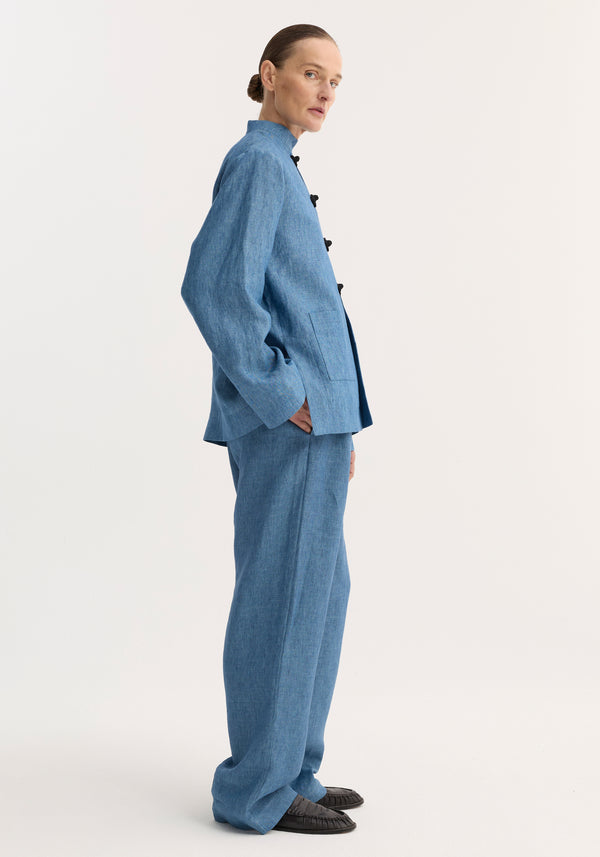 Profile view of person in sky-blue suit, featuring relaxed fit trousers with wide legs and drawstring waistband, styled with black slip-on shoes.