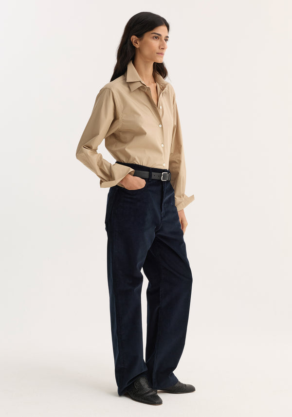 Woman wearing Relaxed corduroy trousers in night, styled with a beige shirt, black belt, and pointed-toe shoes, hand in pocket, looking right.