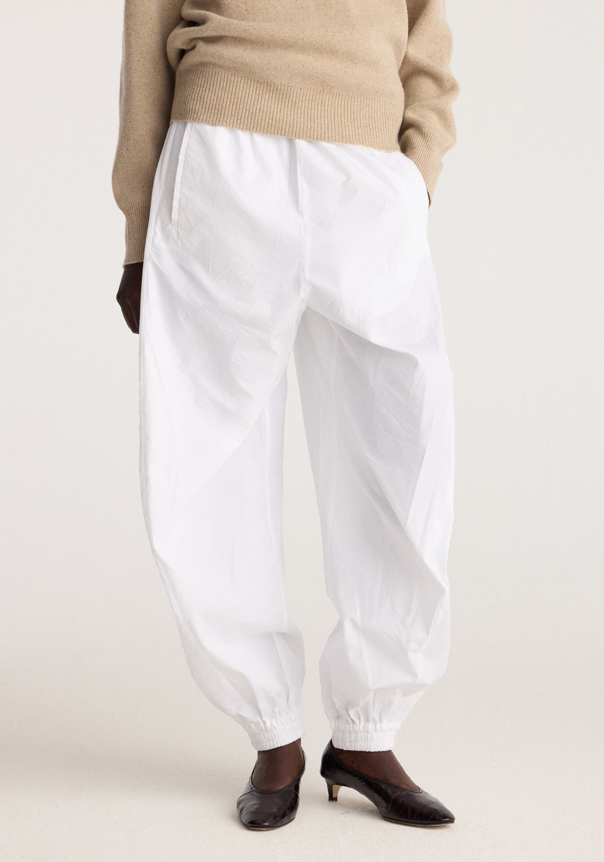 Balloon track pants | optic white worn with a beige sweater, featuring a relaxed balloon silhouette, elasticated ankles, and side pockets styled with black flats