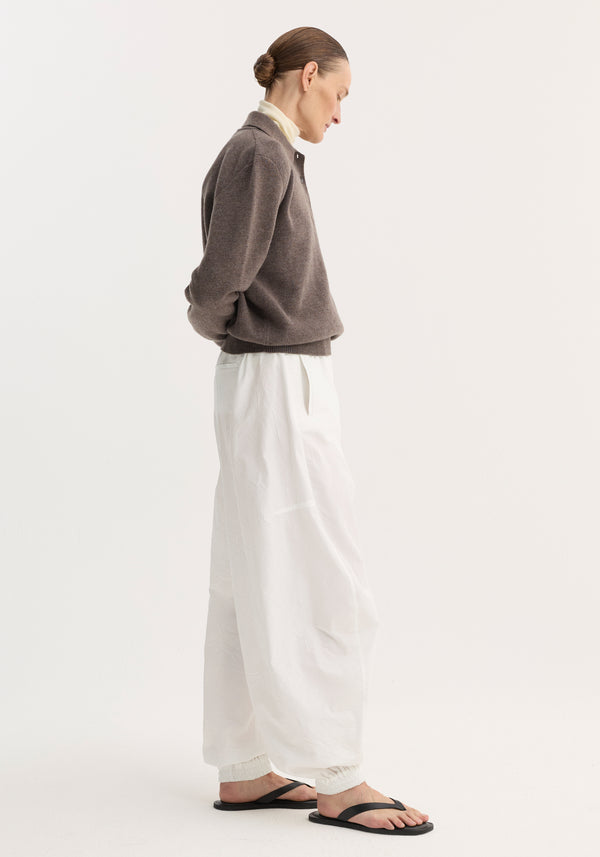 Model in profile wearing Balloon track pants, optic white, featuring a voluminous leg, elasticated waistband, and welt pockets, paired with a dark-gray pullover.
