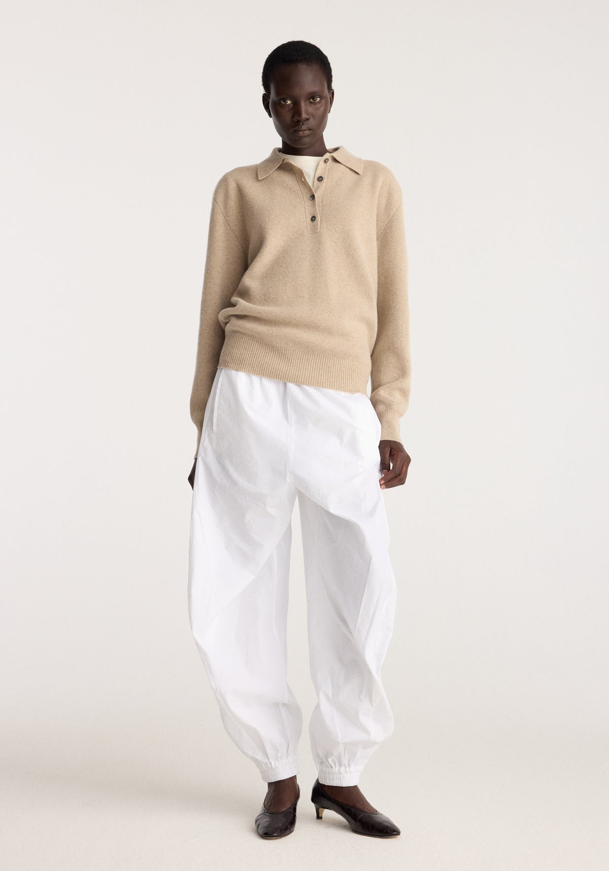 Balloon track pants | optic white worn by a model with a loose fit elastic cuffs and relaxed silhouette styled with a beige knit top and black shoes
