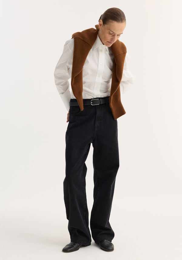 Person in baggy fit denim, black; low-waist, wide-leg jeans with a relaxed style, paired with a crisp button-down and loafers, sweater draped over shoulders.