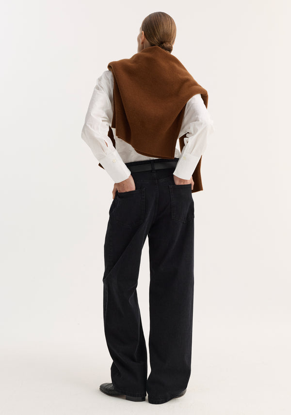 Person in white shirt and brown sweater, showcasing black baggy fit denim with a low-rise, wide-leg design and patch pockets.