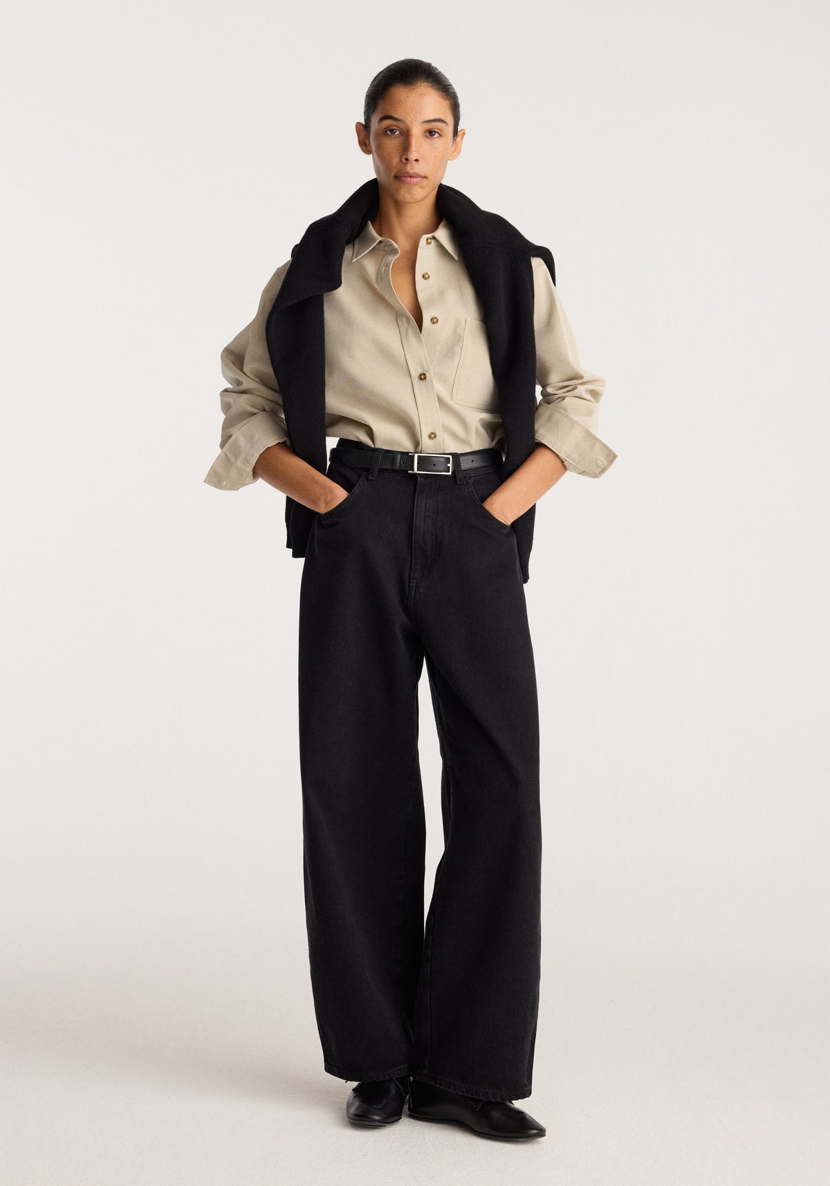 Berber - Barrel leg denim | black worn by a model with a high waist wide barrel leg silhouette and hands in pockets styled with a beige shirt and black shoes