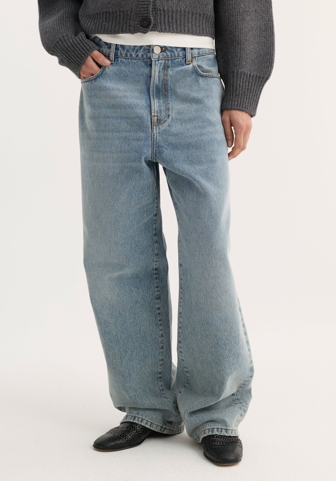 Baggy fit denim in classic blue with wide legs, modeled with one hand in pocket. Paired with a grey sweater and black woven slip-ons.