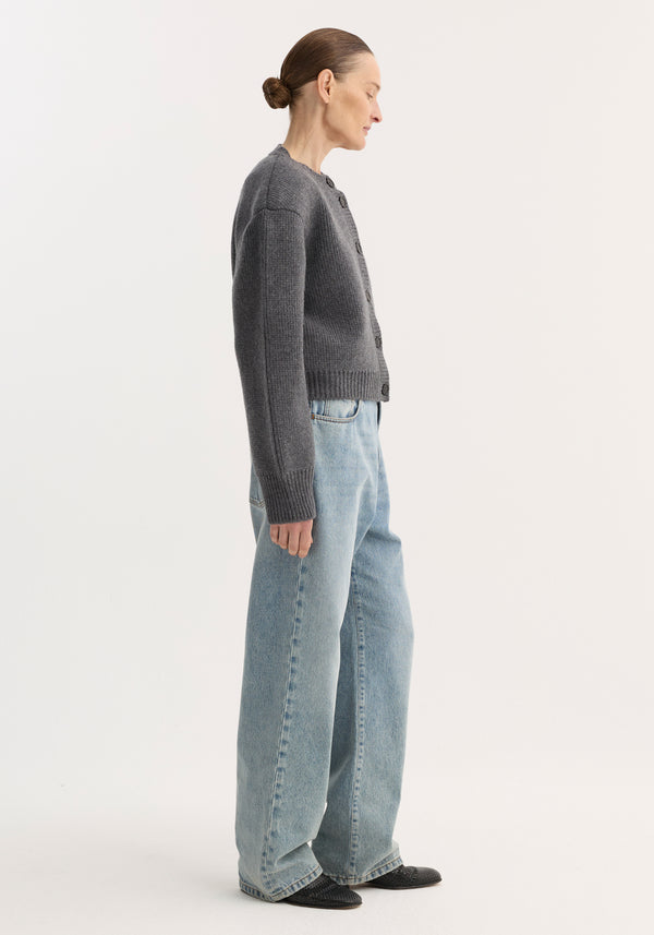 Side-profile of a person wearing Baggy fit denim | classic blue, featuring a low-waist, wide-leg design, paired with a charcoal-gray cardigan and black flats.