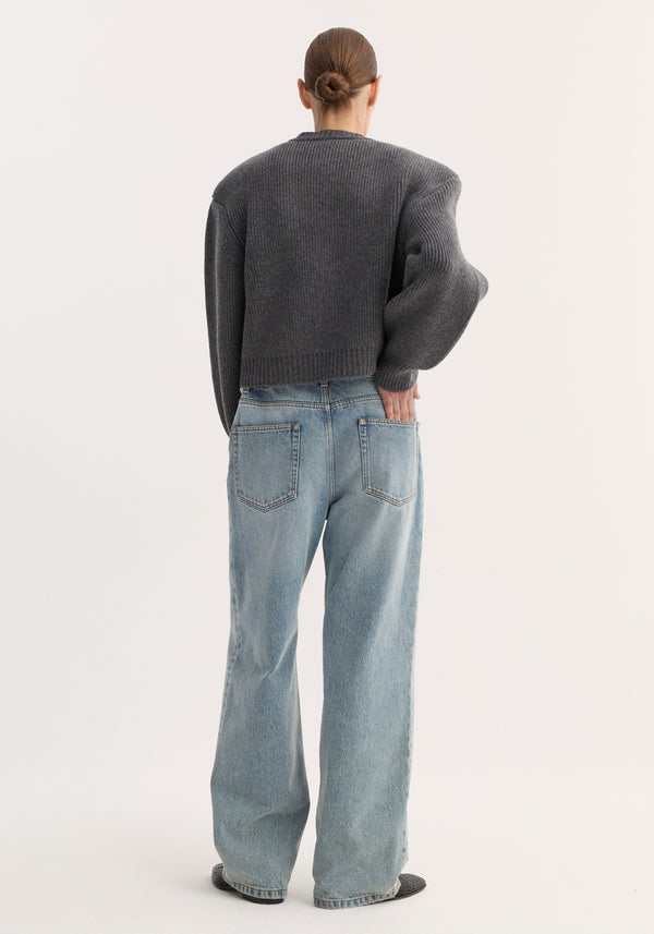 Back view of Baggy fit denim | classic blue with light-wash, high-waisted, wide-leg jeans paired with a charcoal-gray, rib-knit sweater and dark textured slip-on shoes.