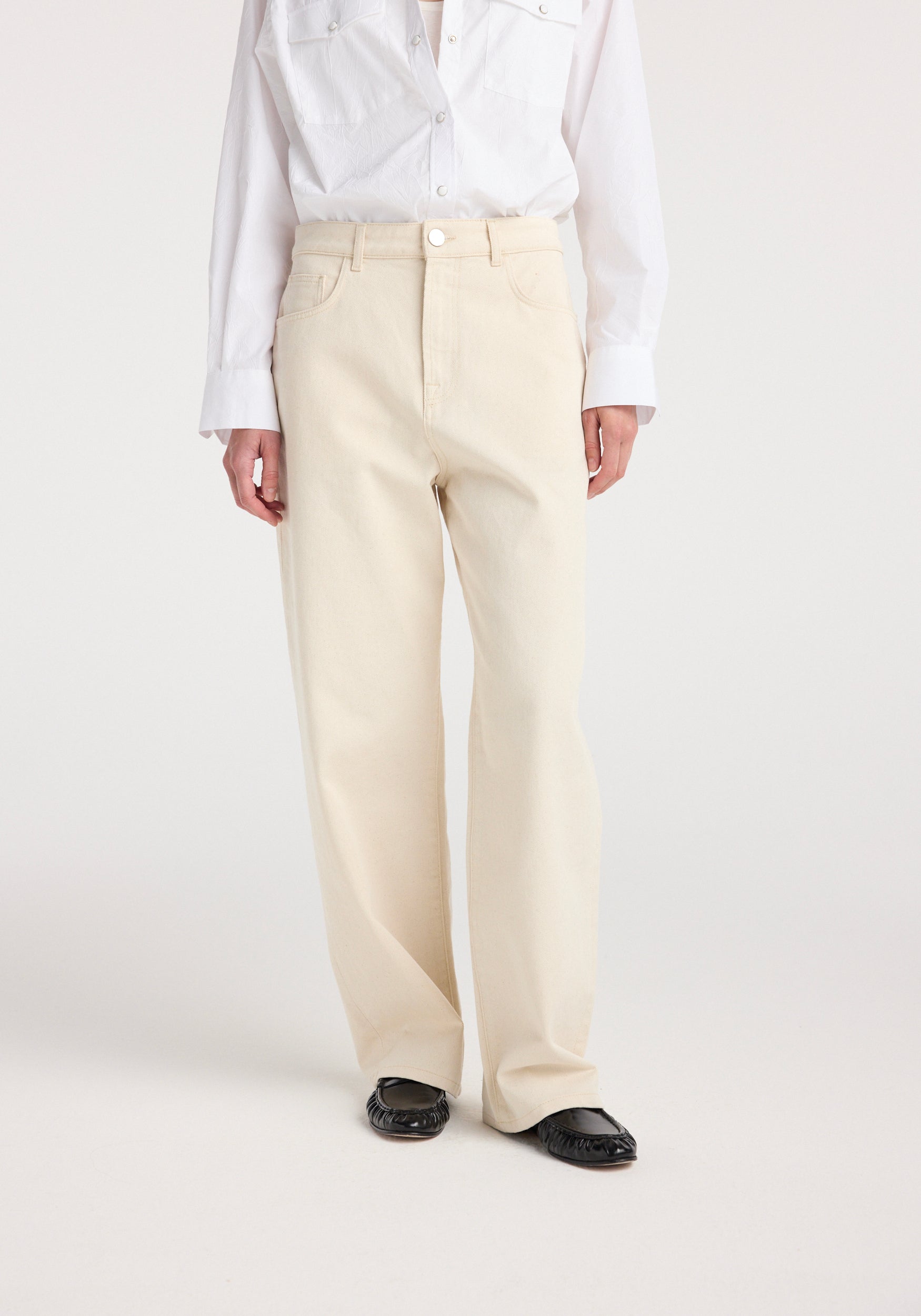 Model wearing Bruun - Signature baggy denim | ecru with a white button-up shirt and black loafers, showcasing the relaxed fit and high waist of the light beige denim jeans.