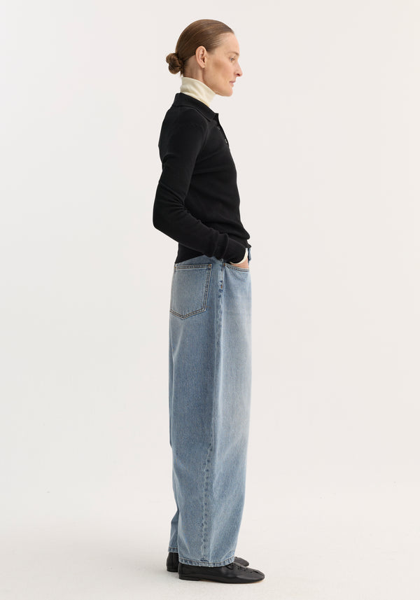 Side-profile of a person in sculptural denim trousers with a balloon leg and high waist, paired with a black knit top and off-white turtleneck.