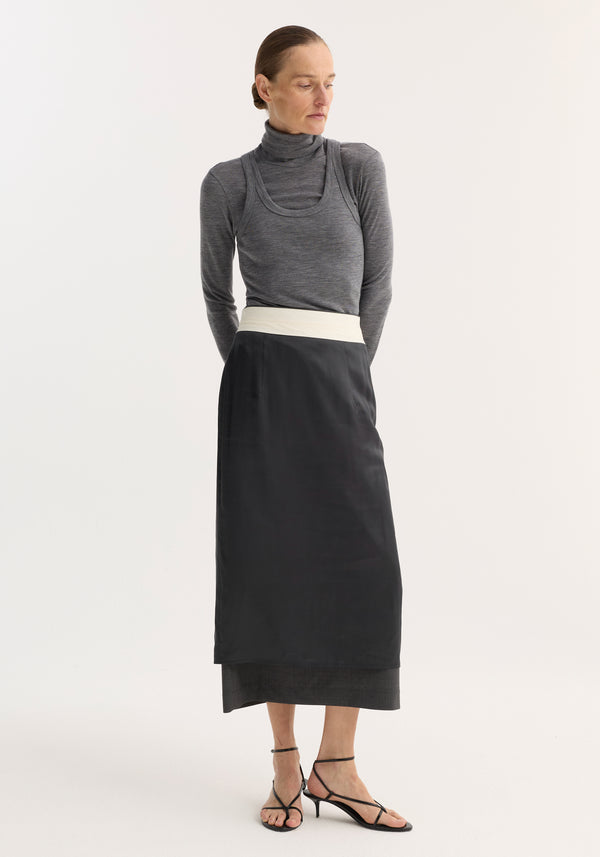Model in Double-layer wool top | mid grey melange, showcasing a turtleneck under a tank, paired with a high-waisted skirt and strappy sandals.