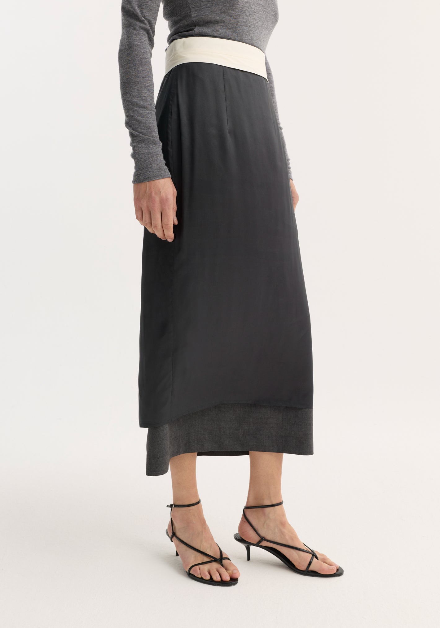 Inside-out skirt in dark grey melange with contrasting off-white waistband, two-layer design, and black heeled sandals, highlighting reversed construction with visible lining.