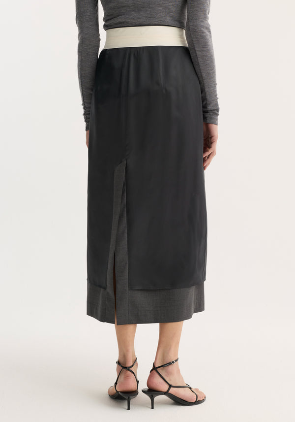 Back view of the Inside-out skirt | dark grey melange, featuring a black outer layer with center slit, exposed lining, and contrast waistband, paired with black sandals.