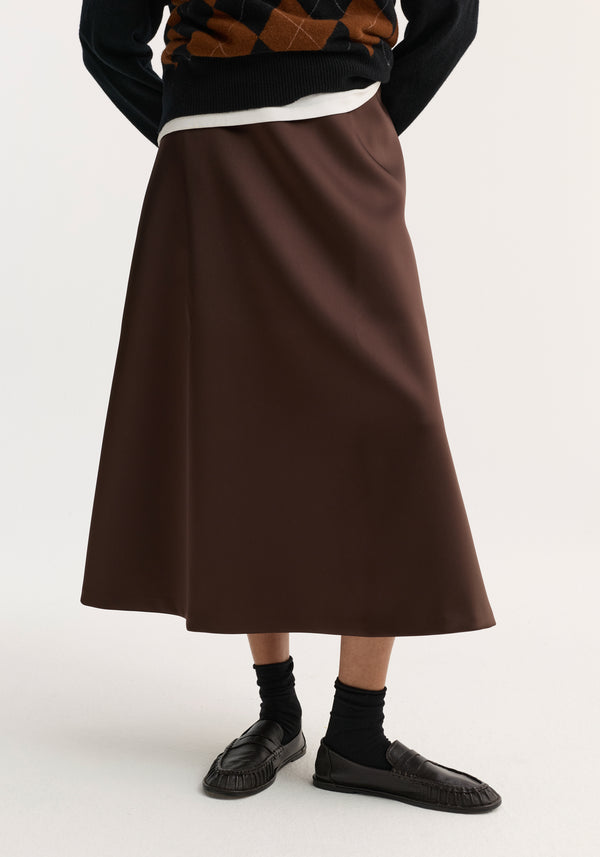 Voluminous A-line skirt in espresso, crafted from heavy satin, mid-calf length, paired with black loafers and socks; sweater and undershirt peek at waist.