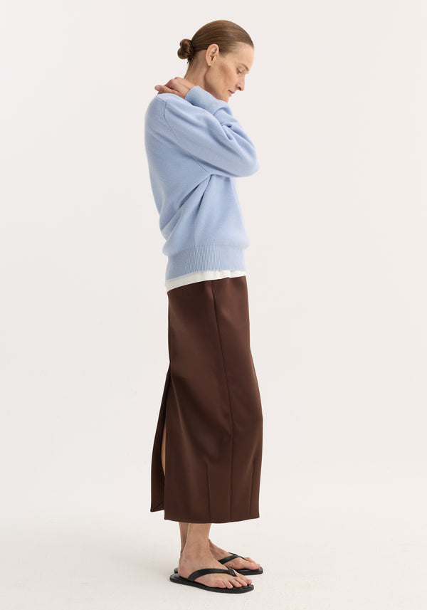 Balloon column skirt in espresso, high-waisted with dart detailing and a side slit, worn with a light-blue sweater and black flip-flops.