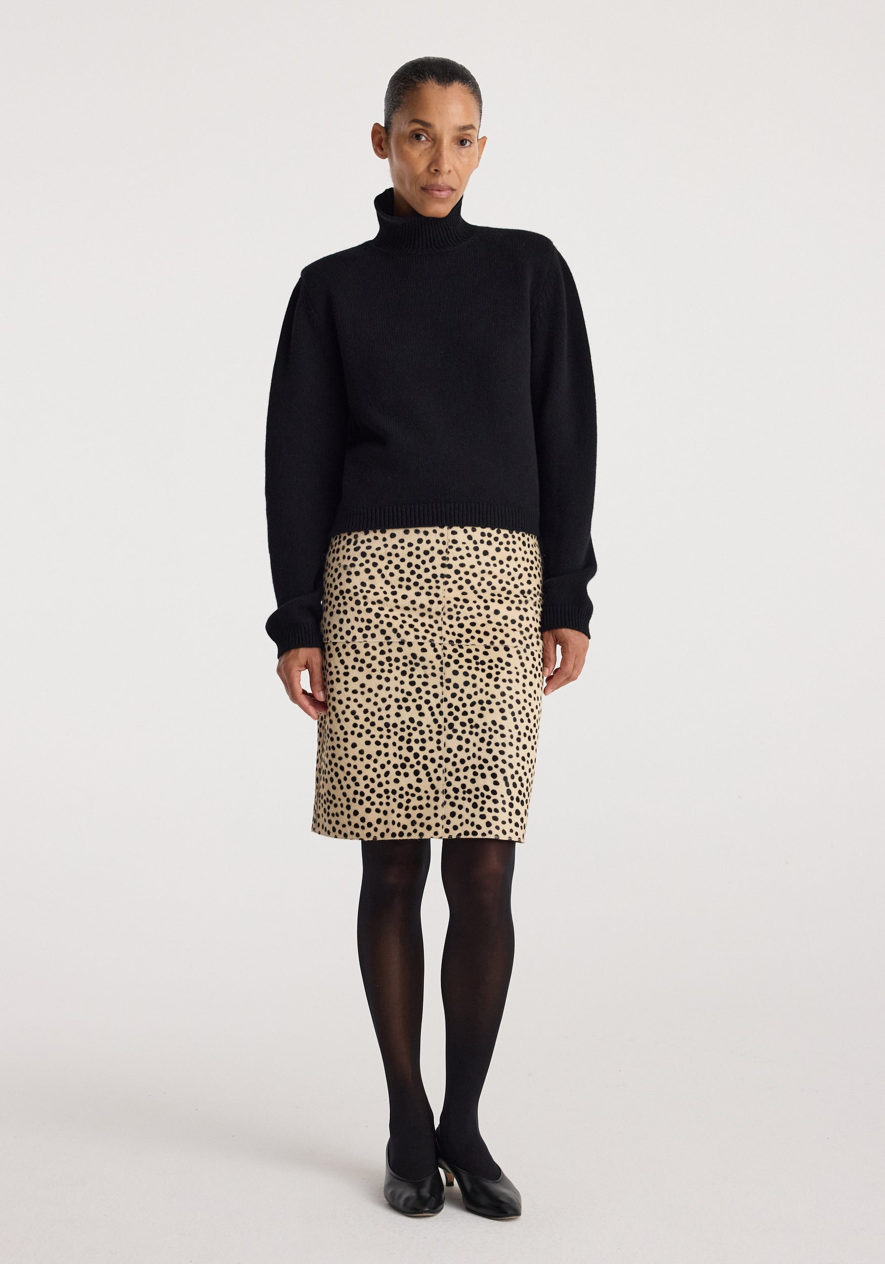 Woman wearing a black turtleneck sweater paired with a beige Pony hair pencil skirt | cheetah featuring a spotted cheetah pattern, black tights, and black shoes.