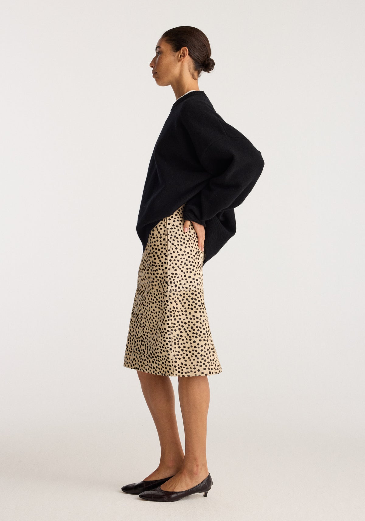 Model wearing Pony hair pencil skirt | cheetah with a black sweater and pointed flats, shown in side profile against a neutral studio background