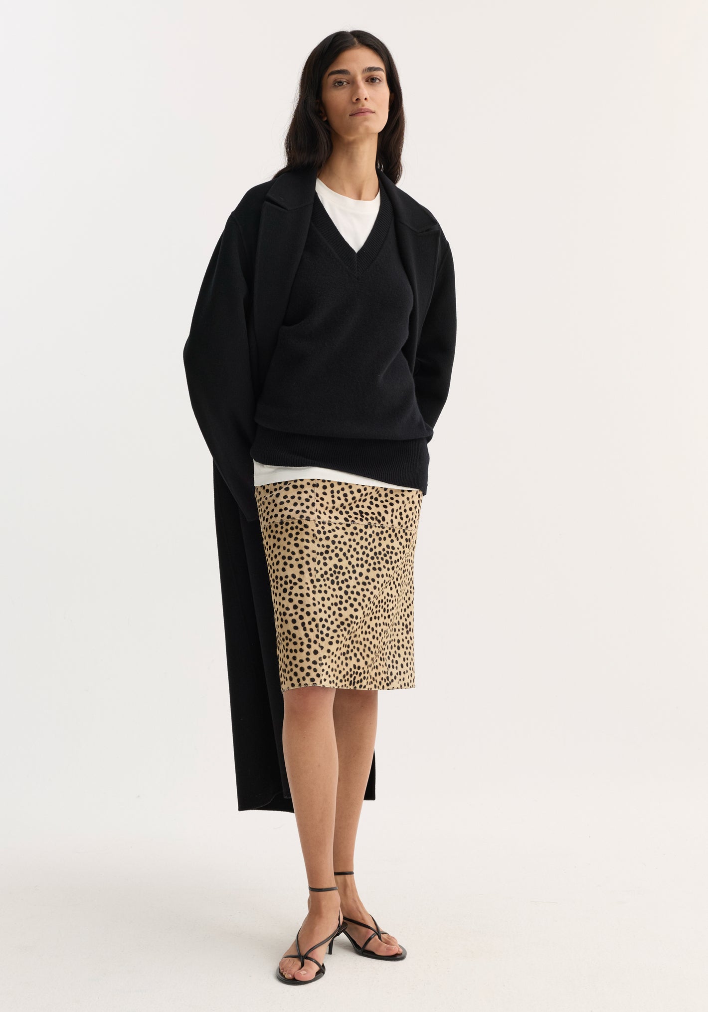 Model wearing a Pony Hair Pencil Skirt in cheetah print, styled with a black cardigan and strappy sandals, showcasing its sleek, knee-length silhouette.
