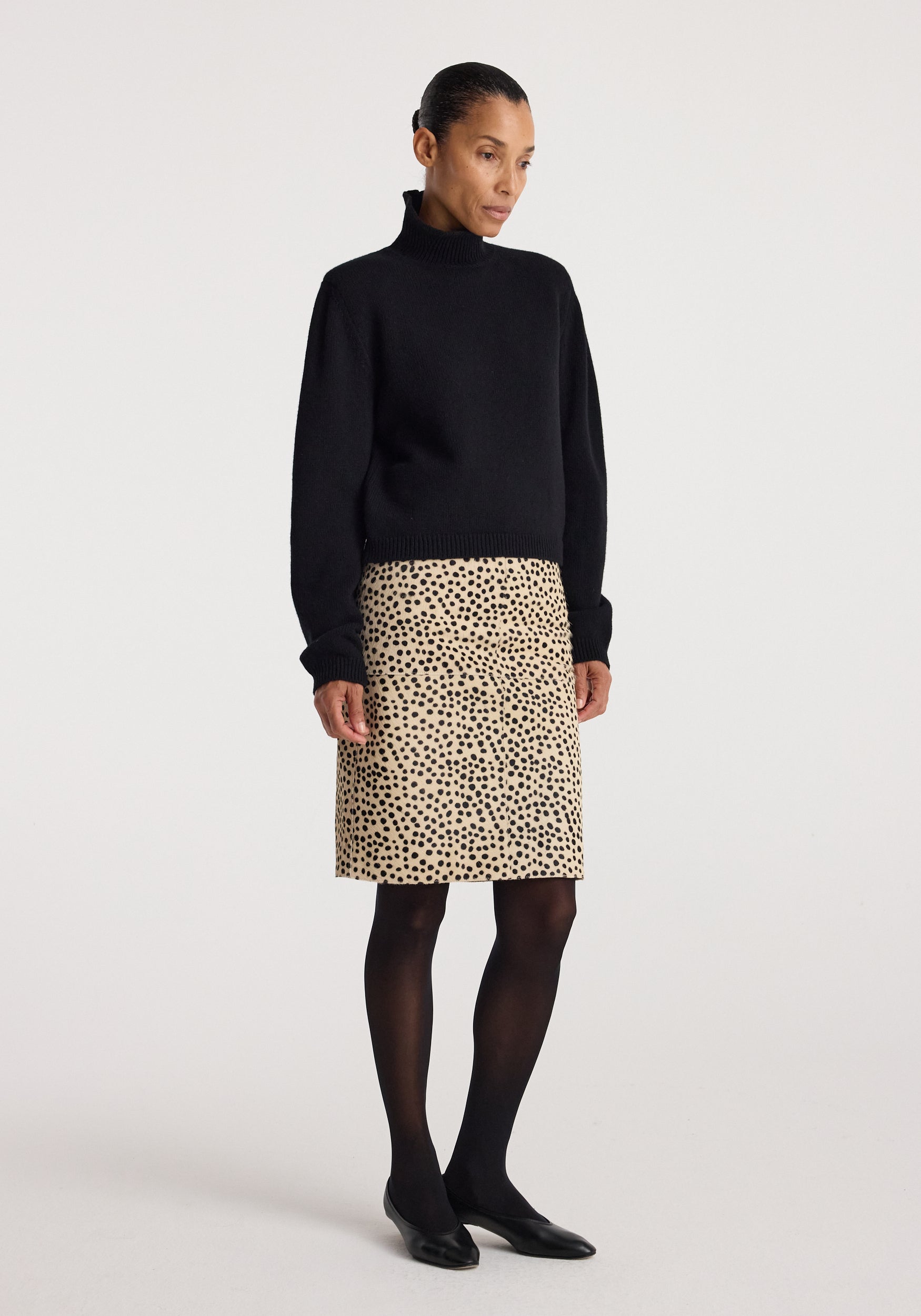 Woman wearing a black turtleneck sweater paired with a pony hair pencil skirt | cheetah featuring a beige base and black cheetah spots, styled with black tights and flats.