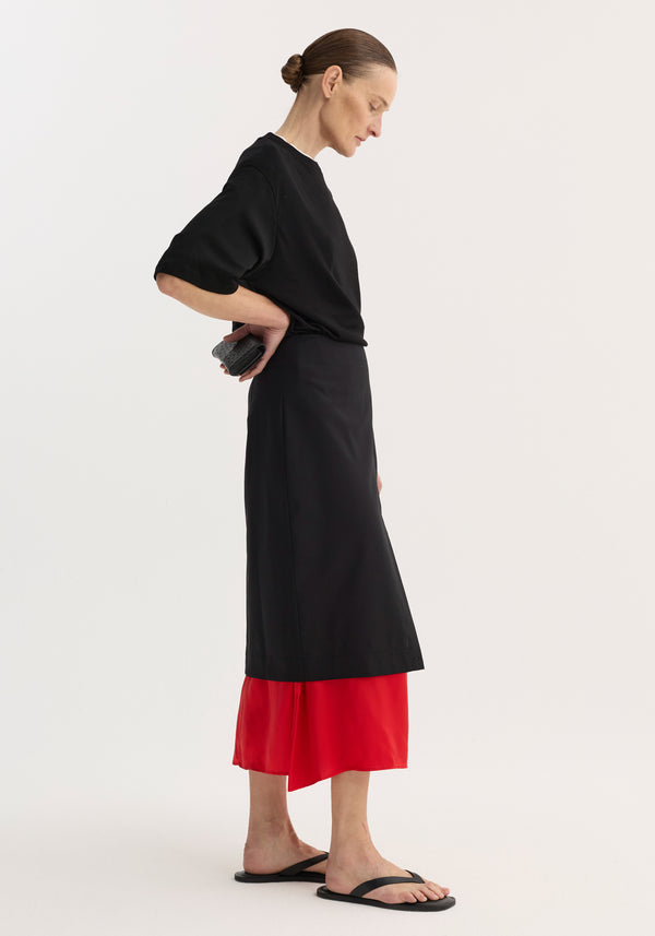 Model in profile wearing Contrast Upside-Down Skirt | Black, featuring a high-waisted, calf-length pencil skirt with red underlay and front slit, paired with a black top.