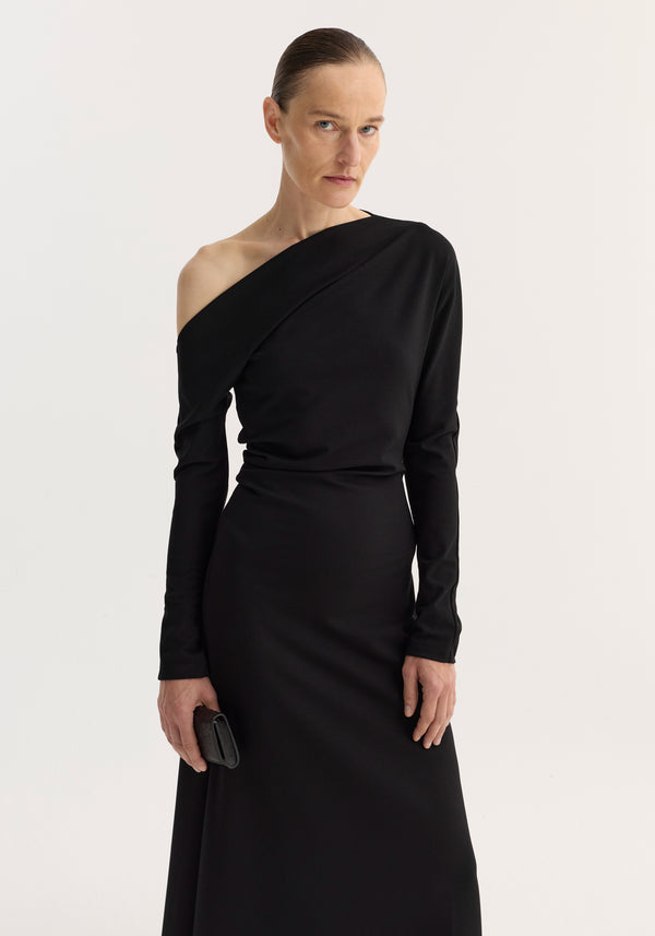 Twisted jersey dress | black: A model in an off-the-shoulder long-sleeve black dress, holding a black clutch, showcasing its elegant drape and asymmetric neckline.