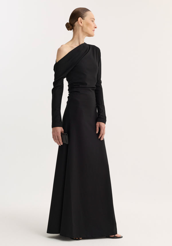 Model in Twisted jersey dress | black, with an asymmetric neckline and long sleeves, holding a clutch. The gown drapes elegantly, highlighting a sculpted silhouette.