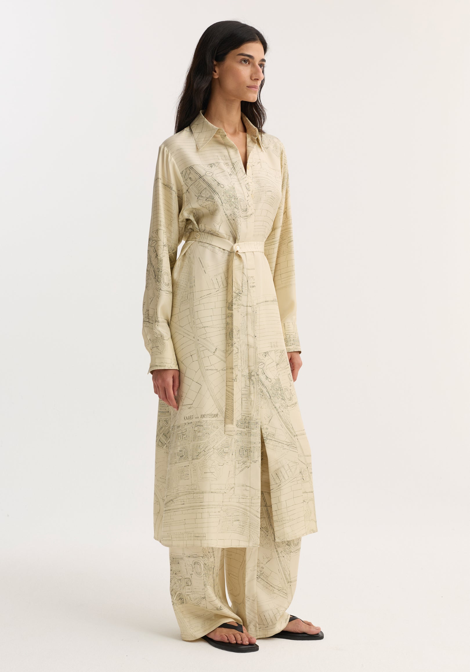Woman wearing Silk open back wrap dress | Amsterdam, featuring map print, classic collar, long sleeves, cinched waist, with matching wide-leg trousers and black sandals.