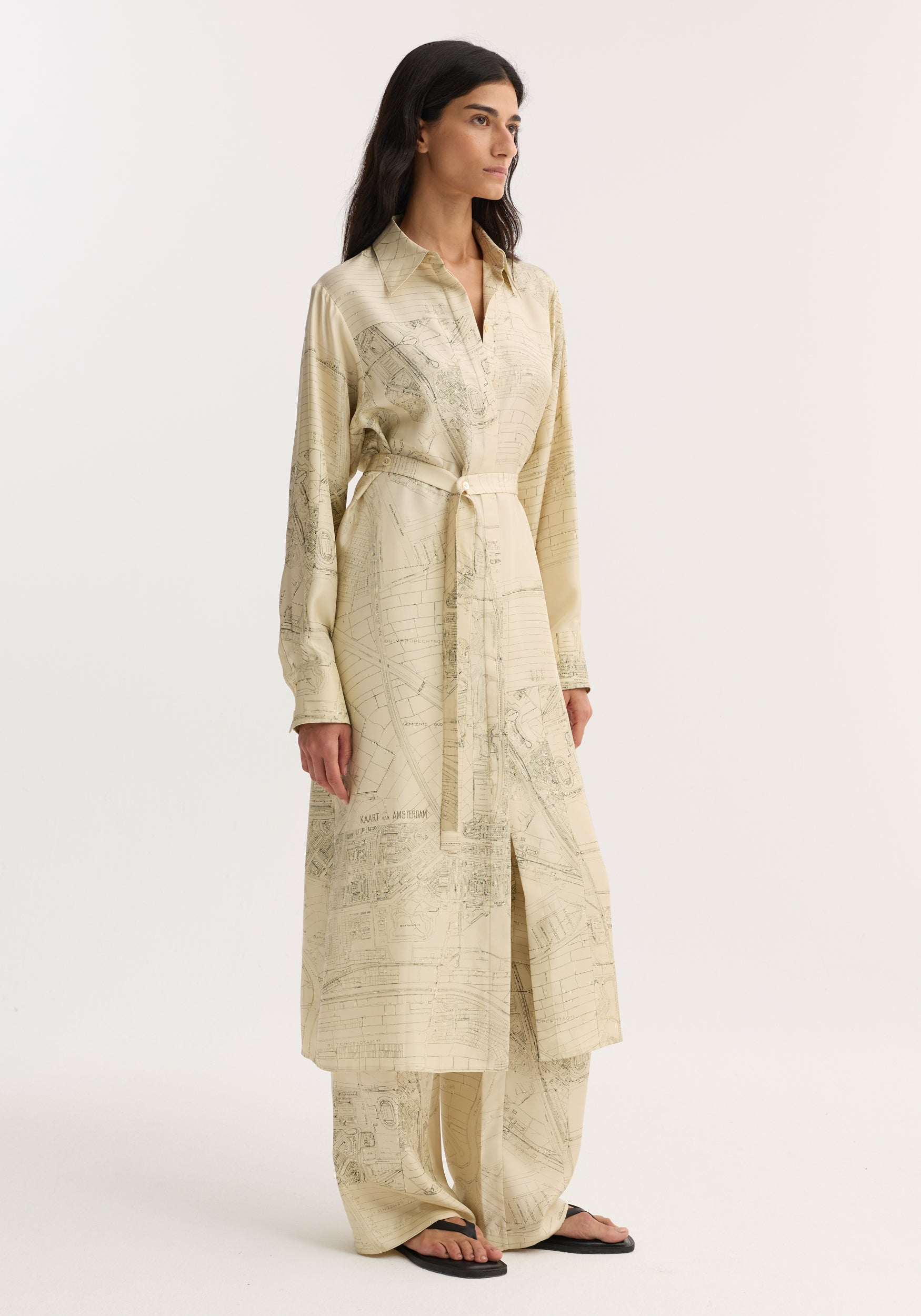 Woman wearing Silk open back wrap dress | Amsterdam, featuring map print, classic collar, long sleeves, cinched waist, with matching wide-leg trousers and black sandals.