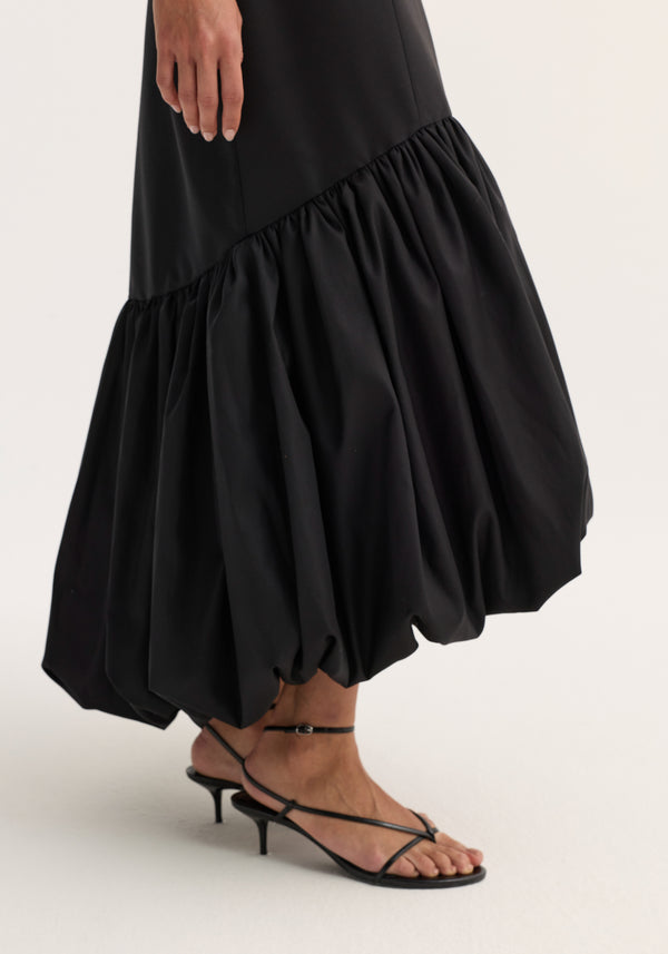Voluminous dress | black, featuring a mid-calf bubble-hem and tailored seam detailing. Paired with black strappy sandals, highlighting its sculptural peplum hem.