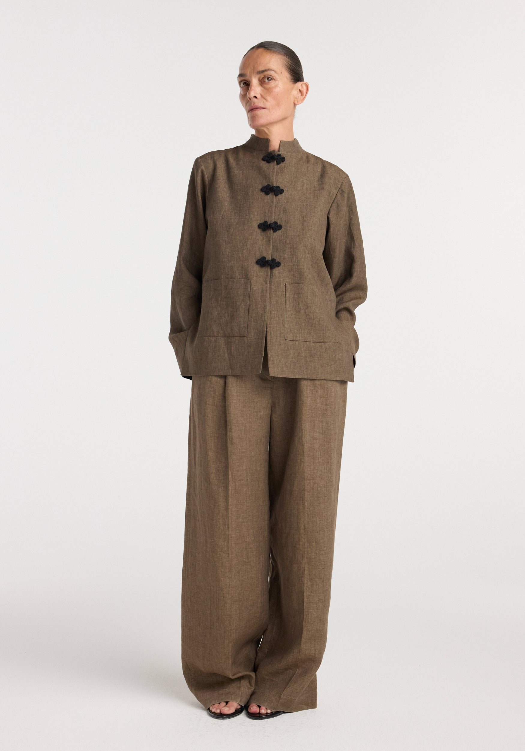 Woman wearing a brown melange linen jacket with Pankou closures, paired with matching wide-leg linen pants, standing against a plain white background.