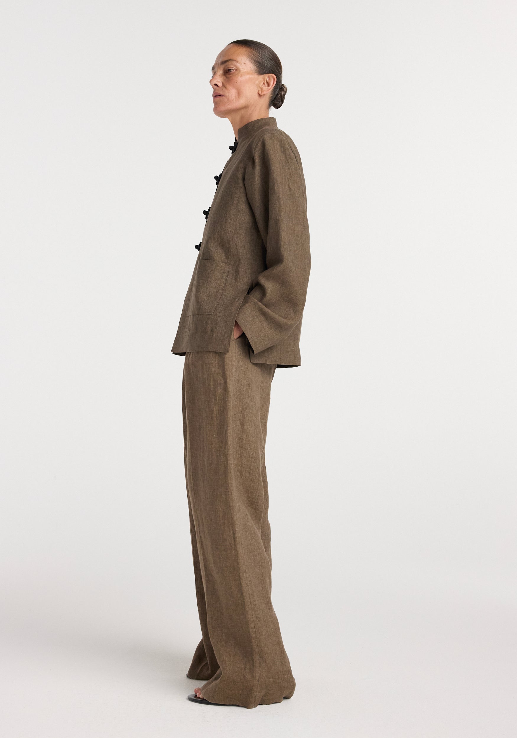 Side profile of a woman wearing a brown melange Pankou closure linen jacket with matching wide-leg pants against a plain background.