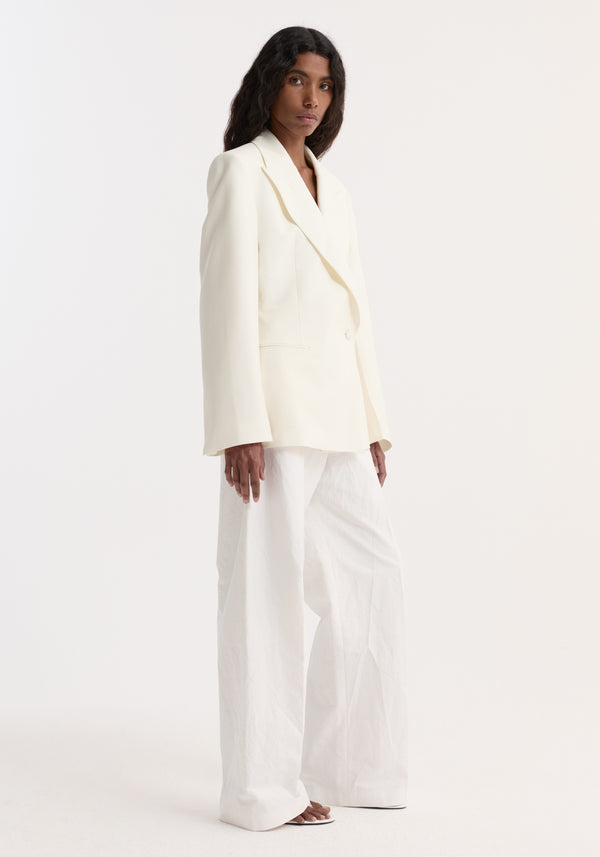 Person wearing an Hourglass shaped blazer in off white with a sharp notch lapel and wide-leg trousers, showcasing a minimalist, structured silhouette.