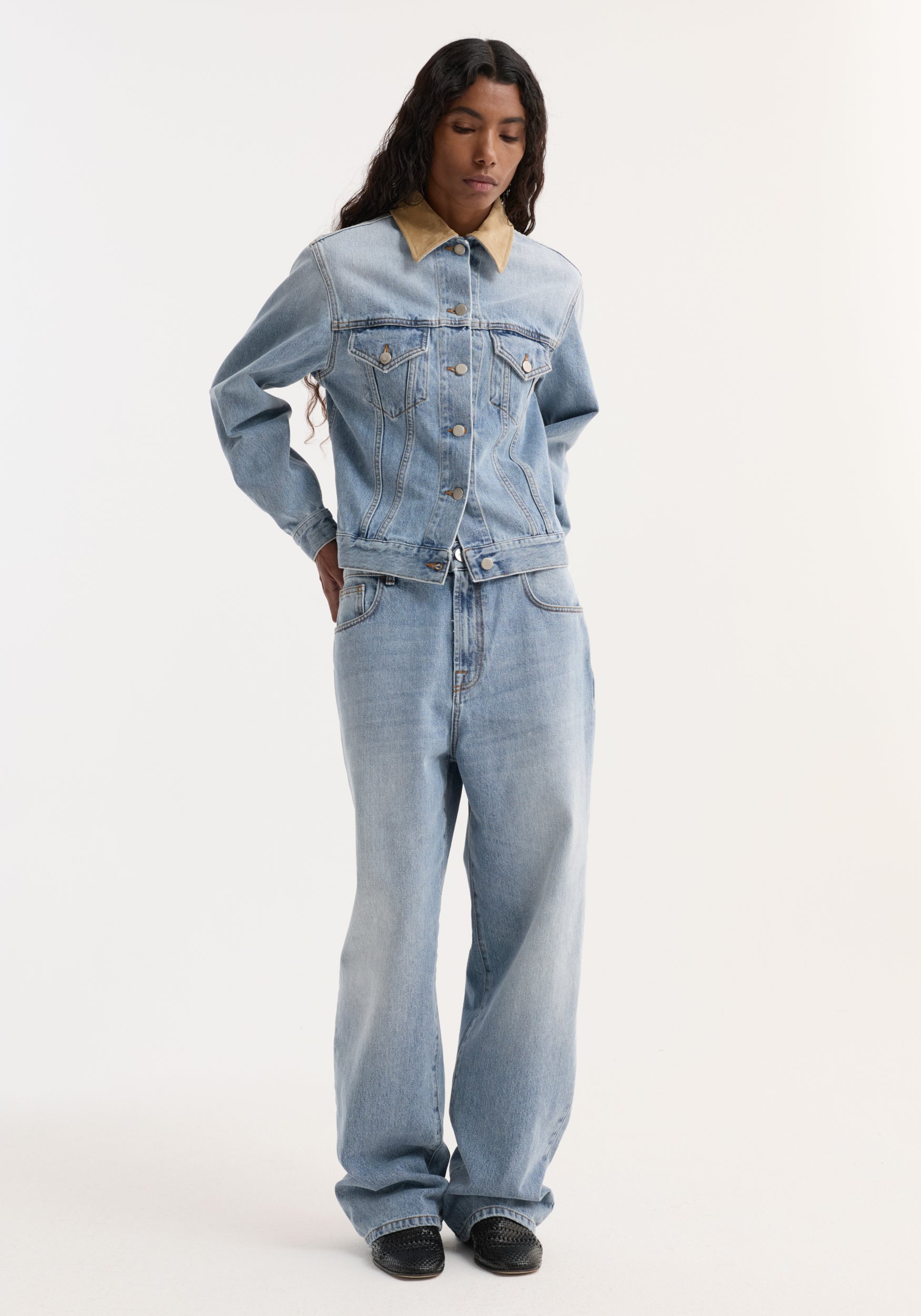 Person wearing Suede collar fitted denim jacket | classic blue, with chest pockets and metal snap buttons, paired with relaxed-fit jeans and black slip-on shoes.
