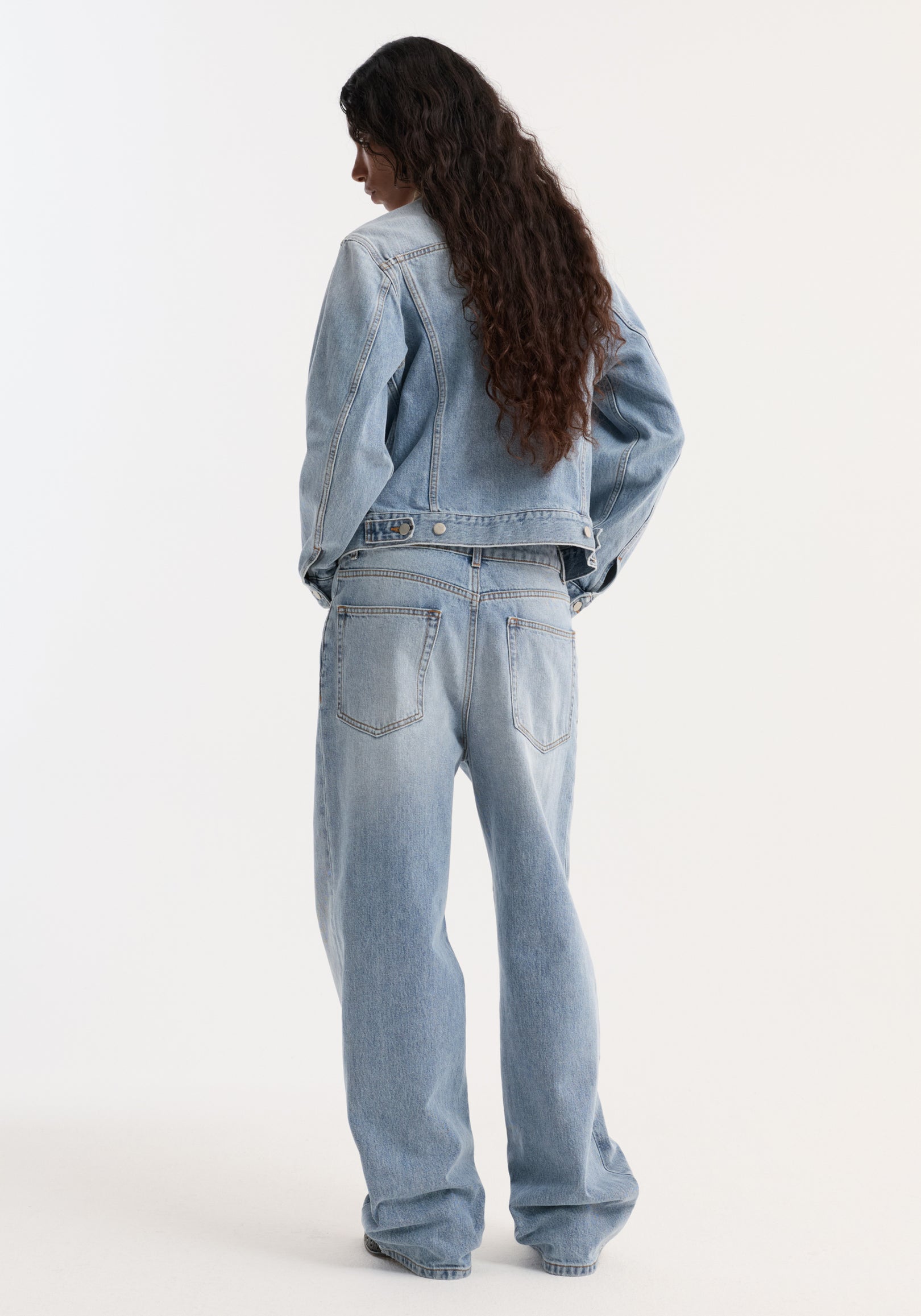 Person in a light-wash, fitted denim jacket with a contrasting suede collar, paired with high-waisted, wide-leg jeans. The jacket features chest pockets.