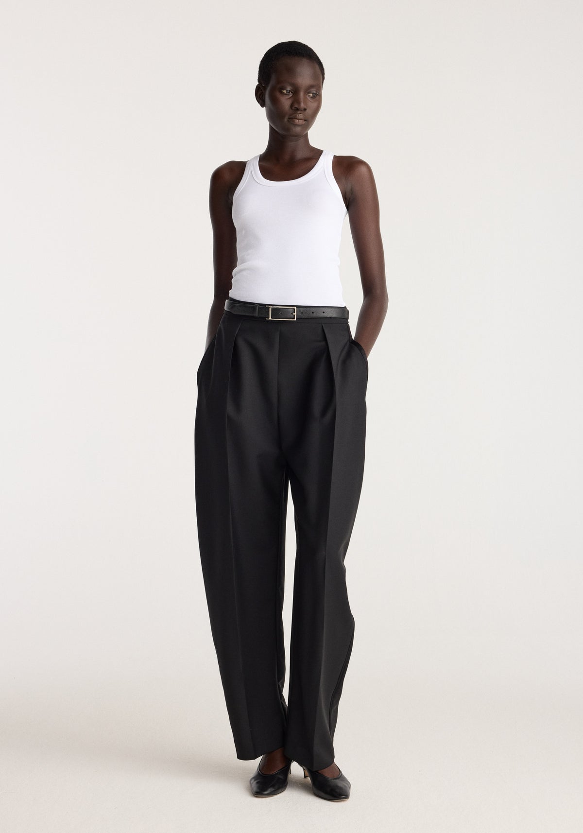 Scoop knitted top | optic white worn by a model with black pleated trousers in a minimalist studio setting