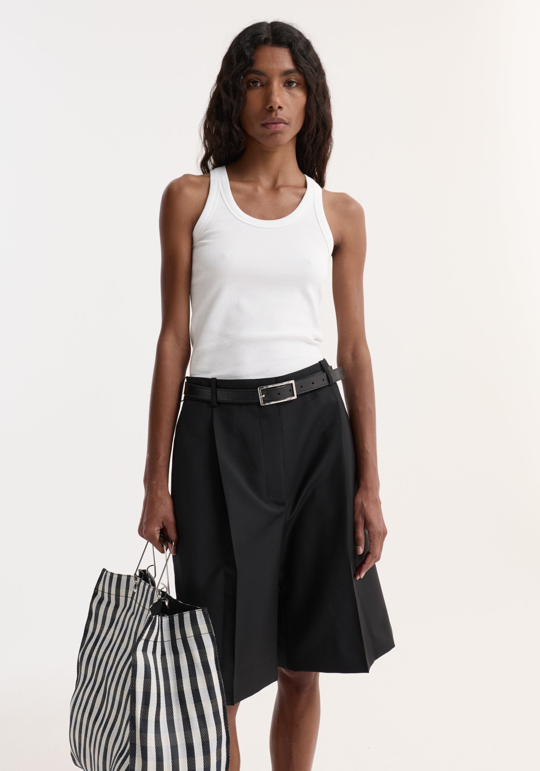 Model wearing the Scoop-neck rib top in optic white with a racerback, paired with pleated black shorts and a striped tote bag.