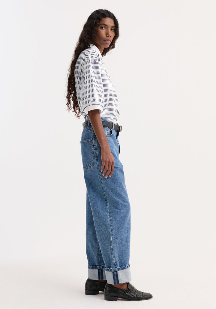 Woman wearing a striped oversized polo with a traditional collar and four-button placket, tucked into high-waisted jeans, styled with a black belt and loafers.
