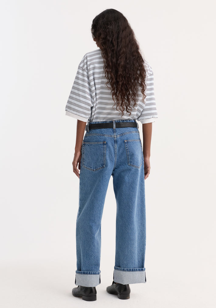 Back view of a person wearing a striped oversized polo with short sleeves, paired with high-waisted jeans, black belt, and low-profile shoes.