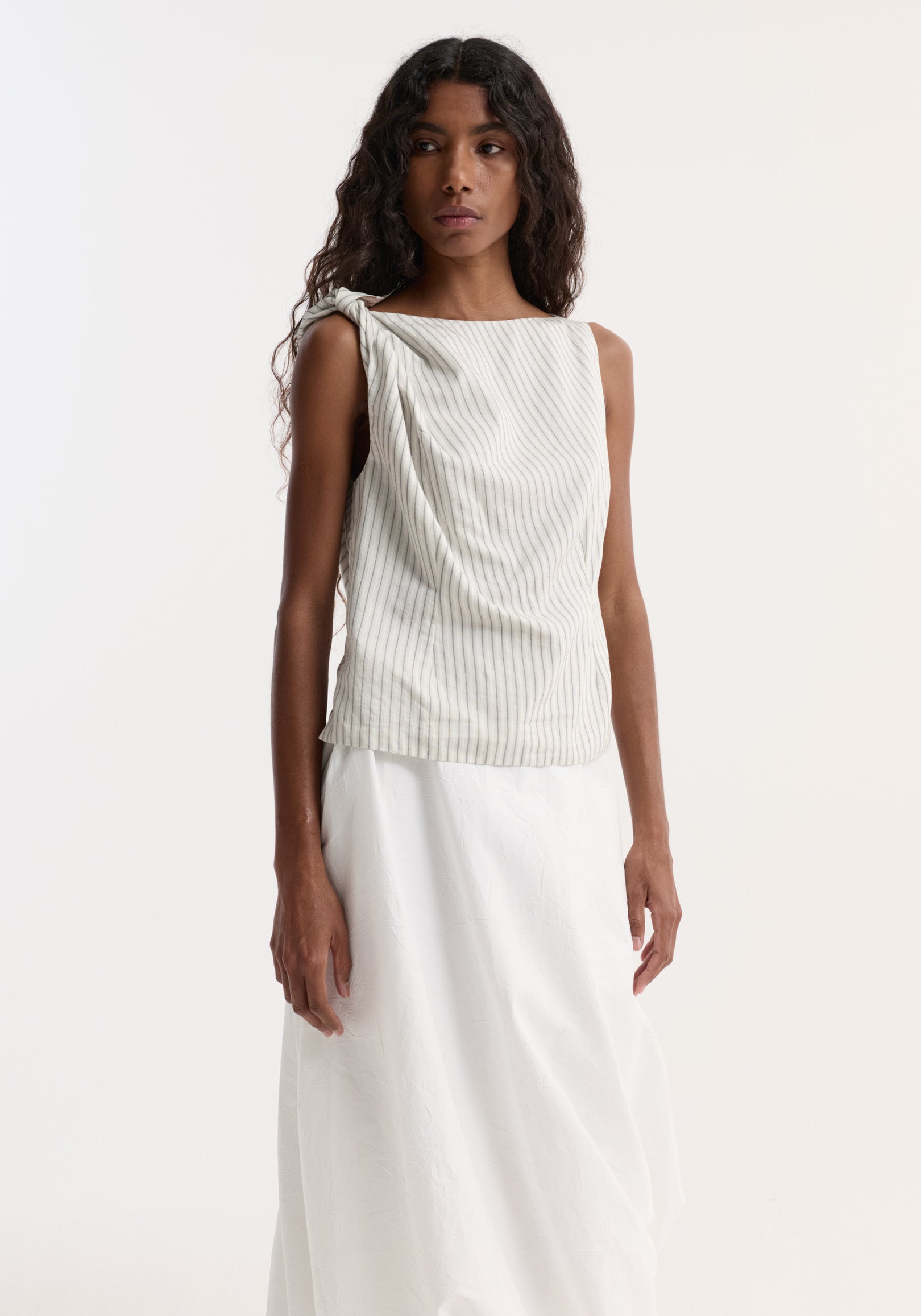 Model wearing Silk-blend draped top | fine stripe with a twist detail at the shoulder, boat neck, and gathered waist, styled with a long skirt.
