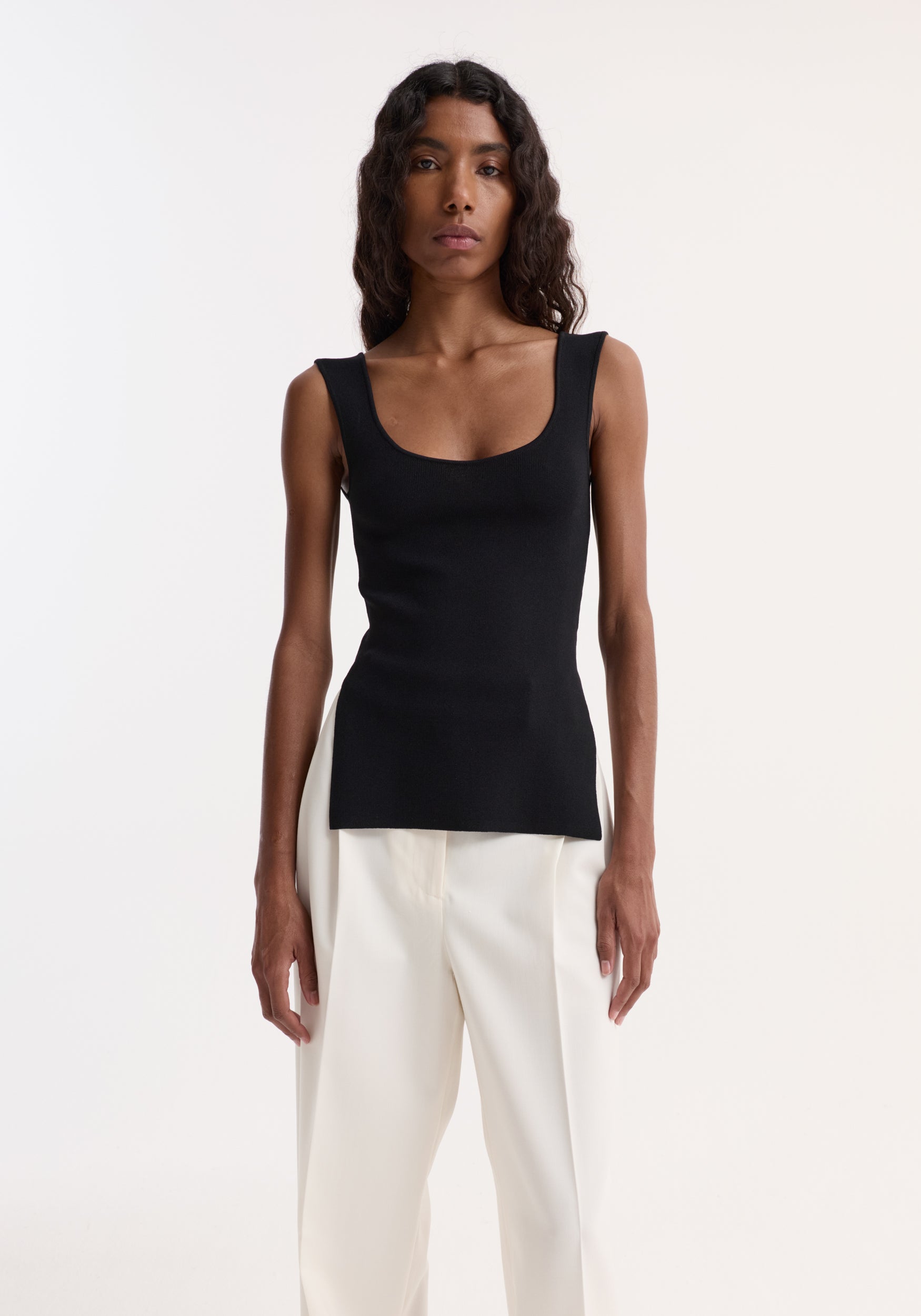 Model wearing the Long knitted bustier top, black, with a scoop neckline, fitted design, elongated silhouette, and side slits, paired with high-waisted trousers.