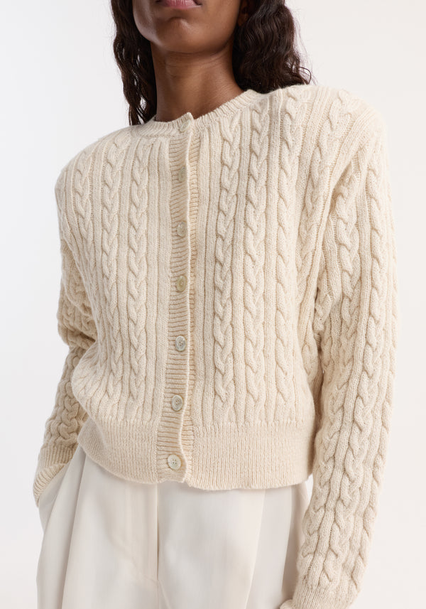 Fine merino cable cardigan in cream, featuring a textured knit with shoulder pads, small buttons, and a slightly cropped fit, worn with matching trousers.