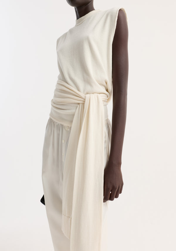 Model wearing Open back knitted wrap top in off-white, featuring sleeveless design, sash-style extensions tied at waist, paired with silky ivory trousers.