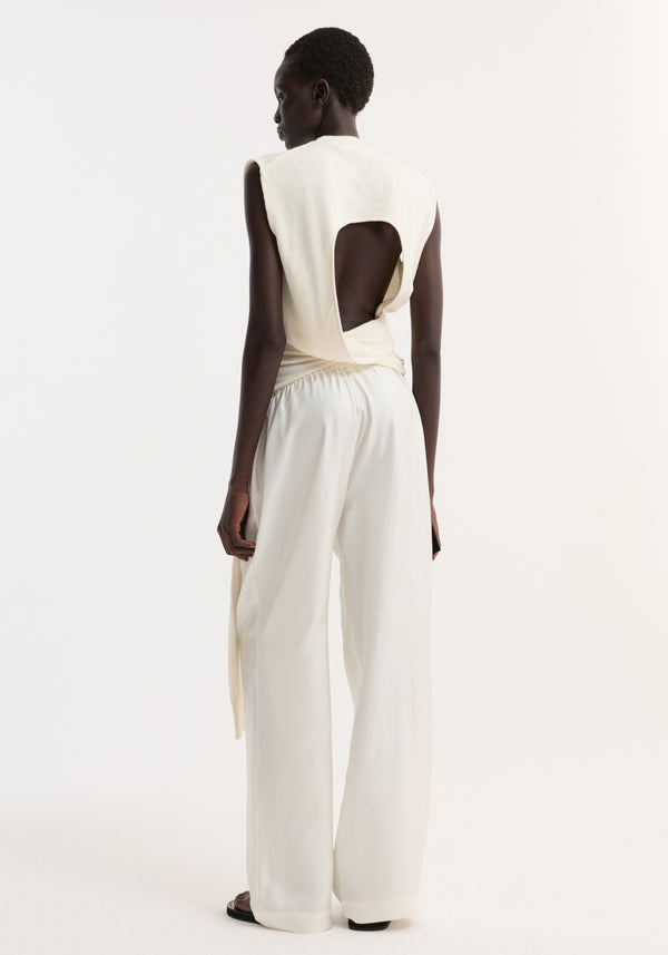 Model in an Open back knitted wrap top, showcasing the dramatic back cutout, draped tie detail, and wide-leg trousers, highlighting minimalist design and clean lines.