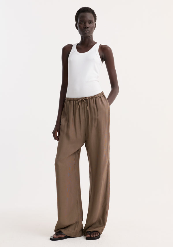 A person wearing Relaxed fit trousers | brown mini check, featuring a loose fit, drawstring waistband, and side seam pockets, paired with a white tank top.