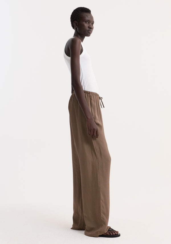Side-profile of model in relaxed fit trousers with a mini check pattern, featuring a wide leg, drawstring waistband, and side seam pockets, styled with a white tank top.