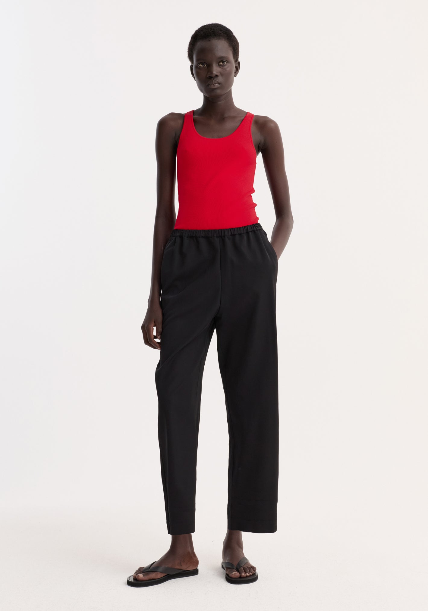 Cropped wide leg trousers in black, featuring an elasticated waist and side pockets, worn with a casual red tank top and black sandals.