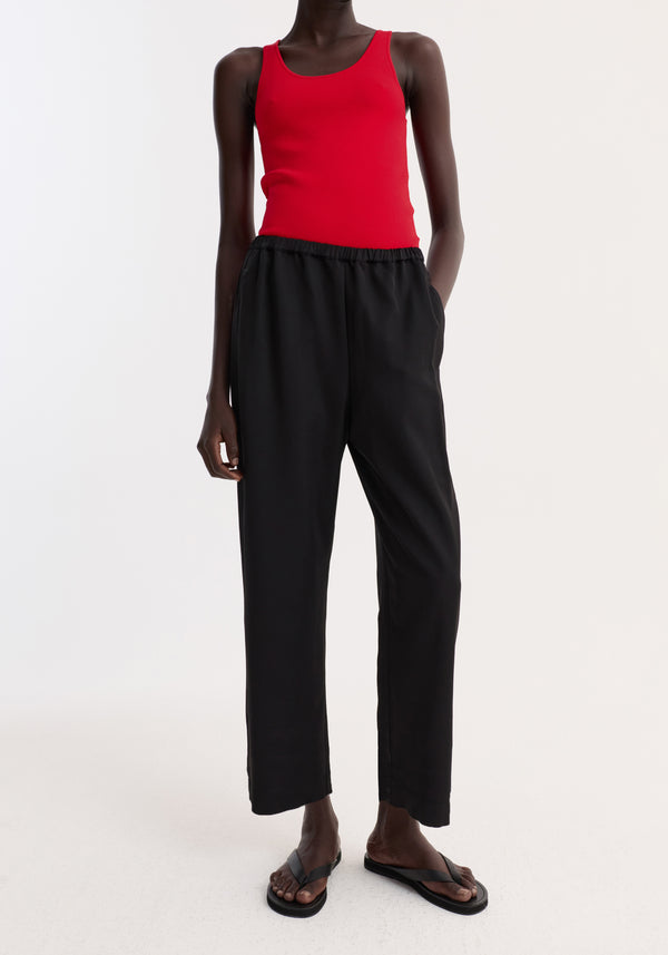 Cropped wide leg trousers | black, featuring an ankle-length, elasticated waist, and side pockets, worn by a model with one hand in the pocket.