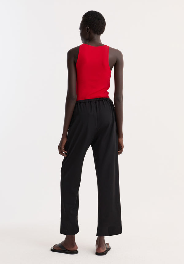 Person wearing cropped wide leg trousers in black, featuring an elasticated waist and ankle length, viewed from behind with a sleeveless top and slide sandals.
