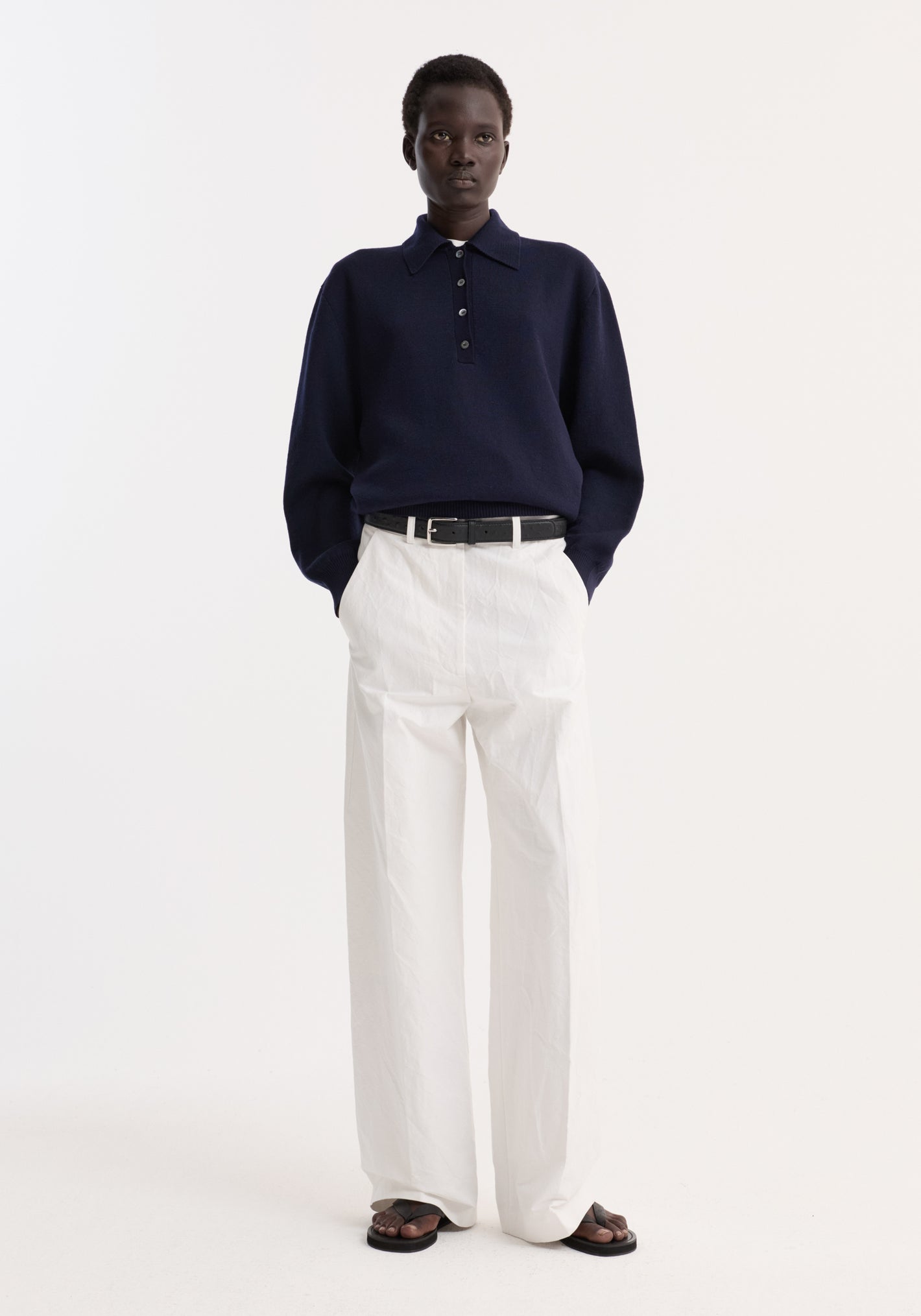 Model wearing Classic loose fit chino in optic white, featuring a baggy relaxed fit with side pockets, tailored waistband, and elongated legs, styled with a navy knit top.