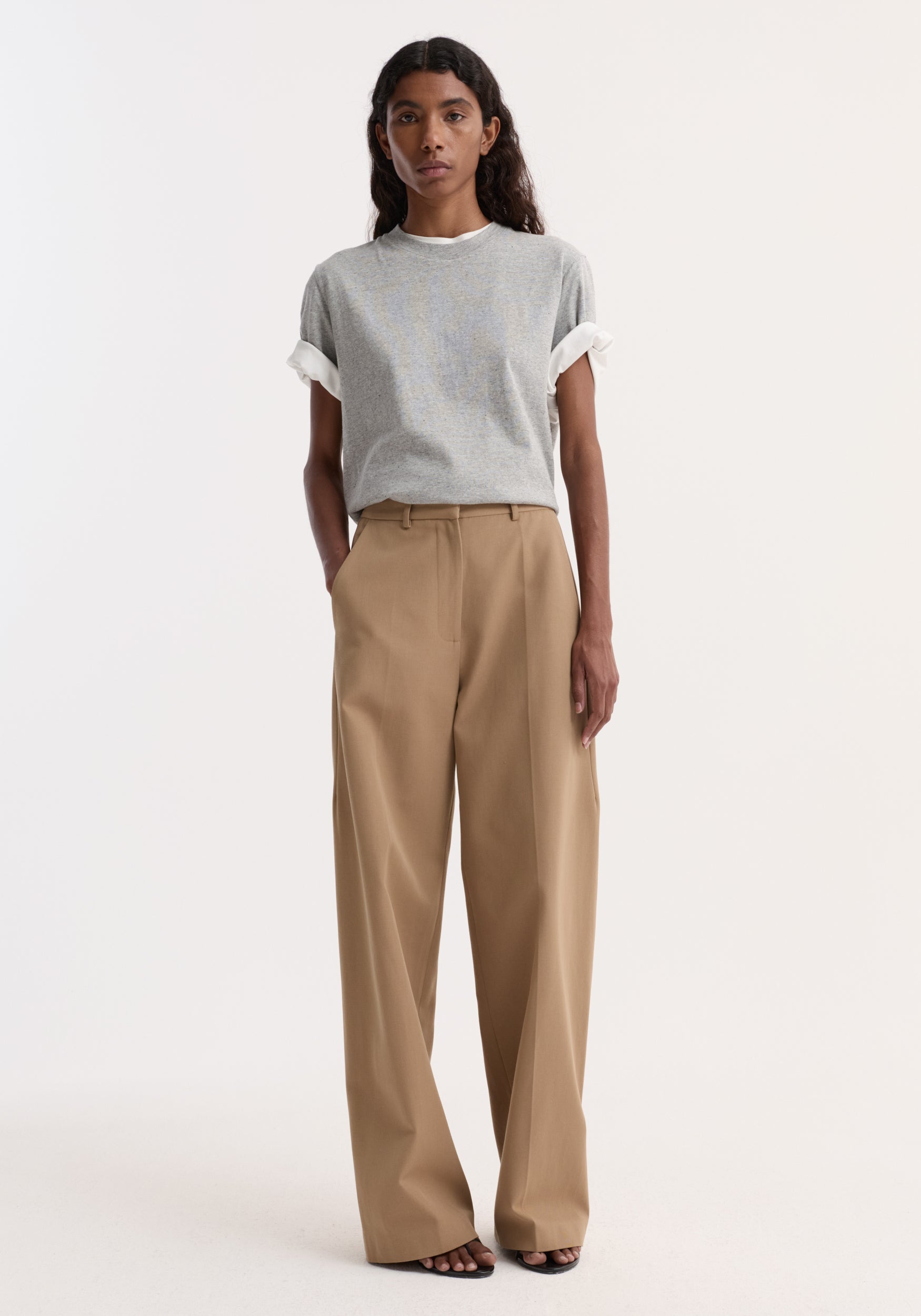 Model wearing Classic loose fit chino | beige, featuring a relaxed fit with side pockets and a tailored waistband, paired with rolled-up gray T-shirt and black sandals.