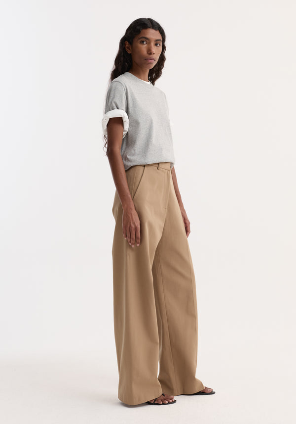Woman wearing Classic loose fit chino | beige, with high-waisted, wide-leg design, tailored waistband, and side pockets, paired with a heather-gray T-shirt and black sandals.
